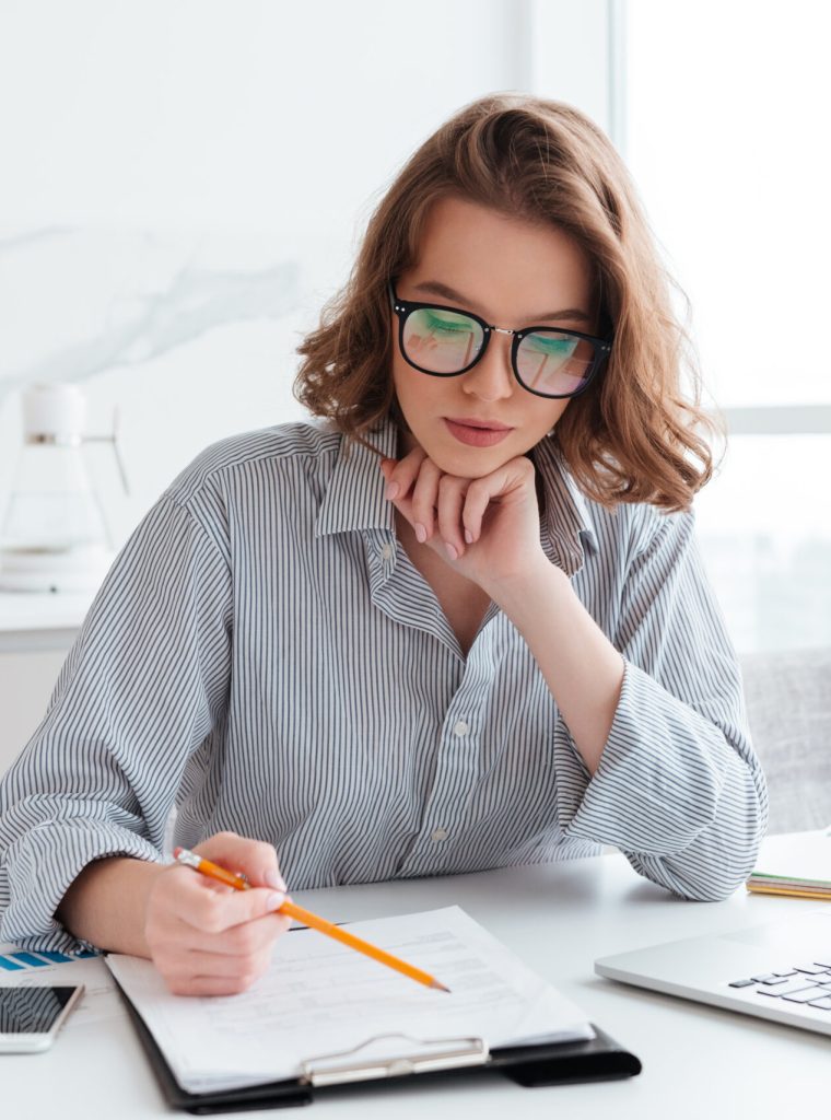 Young concentrated businesswoman in glasses and striped shirt working with papers at home